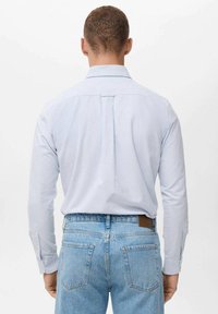 Camisa de rayas azul claro de manga larga con cuello clásico, pliegue trasero único y puños con botones, combinada con jeans de mezclilla azul claro.