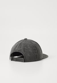 Mørk grå, vasket bomullsbasketcap med justerbar stropp, sett fra baksiden på en hvit overflate.