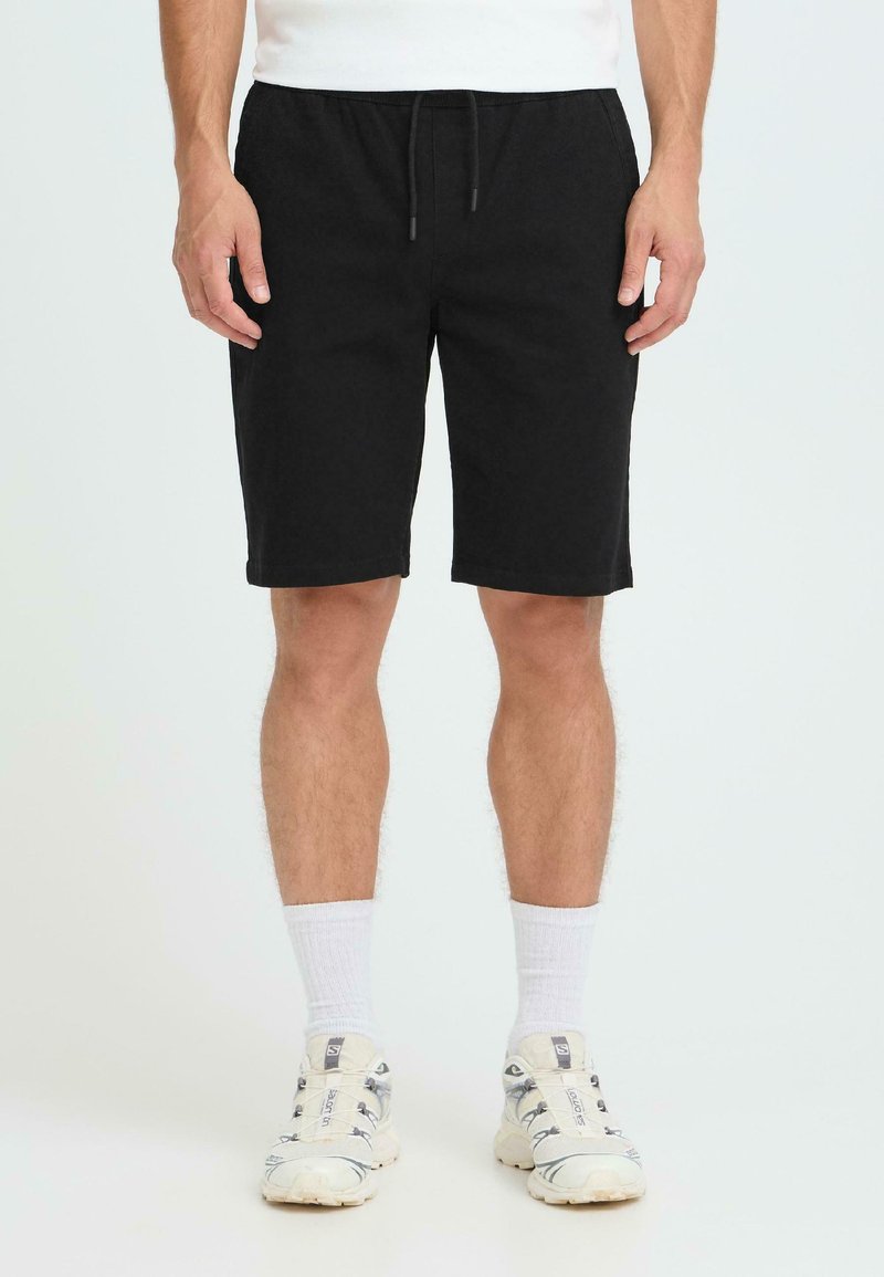 Shorts en coton noir avec une ceinture élastique et un cordon de serrage ; longueur jusqu'au genou, avec une texture lisse et sans motifs ni accents visibles.