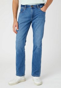 Light blue denim jeans with a straight leg design, five pockets, and a brown button closure at the waist. Features subtle fading.