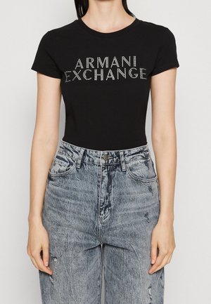 Czarny bawełniany t-shirt z napisem "ARMANI EXCHANGE" ozdobionym srebrnymi ćwiekami, zestawiony z wysokim stanem wyblakłych jeansów.
