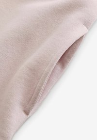 Vaaleanpunainen neulekangas, jossa on sileä pinta, erityisellä kääntöreunalla ja huomaamattomilla ompeleilla, esittelee pehmeän ja mukavan muotoilun.