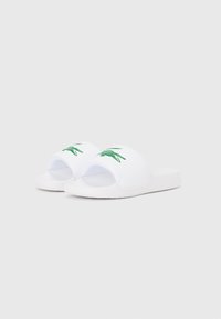 Άσπρα σανδάλια τύπου slip-on με ανοιχτό σχεδιασμό στα δάχτυλα, που διαθέτουν πράσινο λογότυπο κροκοδείλου στο επάνω μέρος. Μαλακό υλικό με υφή στην σόλα.