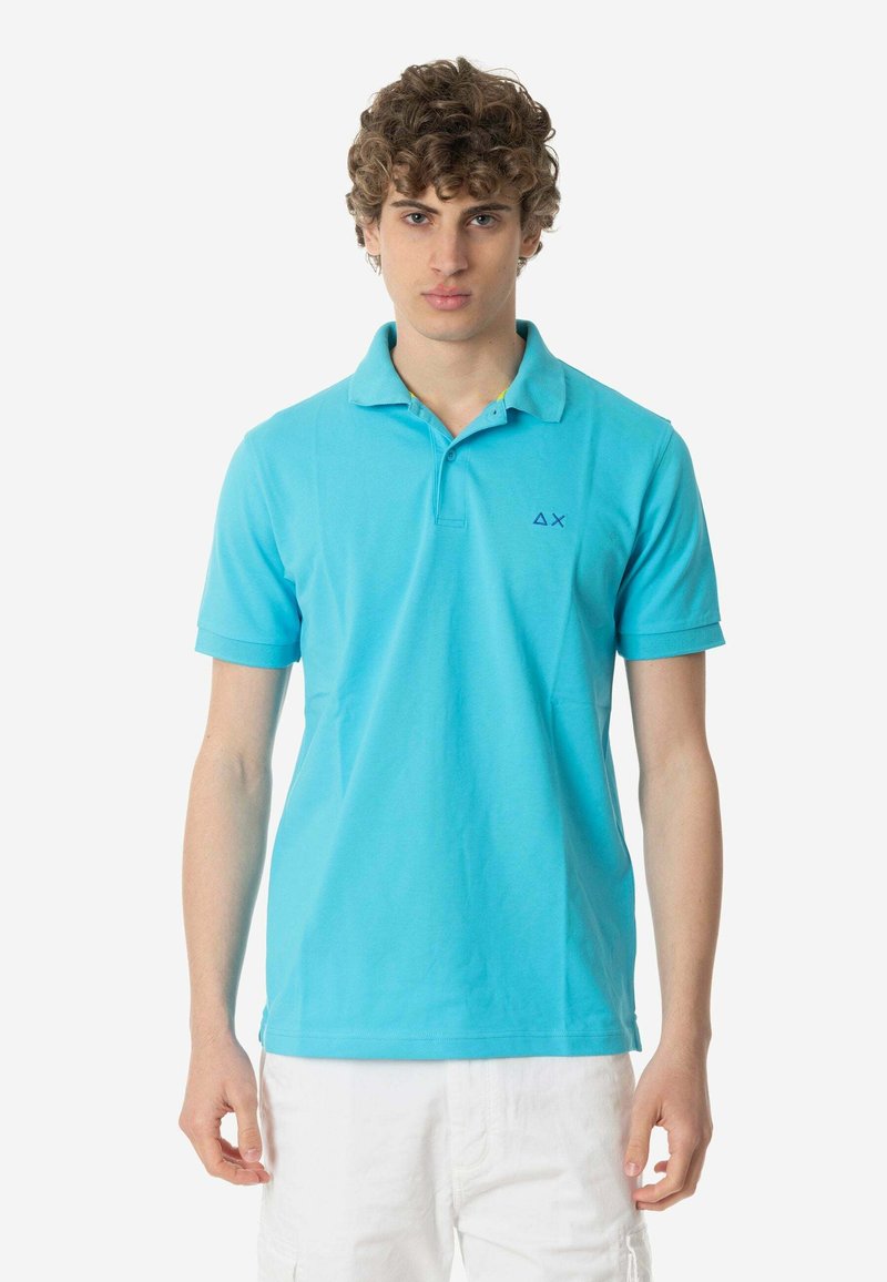 Polo shirt turchese in cotone, con colletto tradizionale, maniche corte e un piccolo logo blu scuro sul lato sinistro.