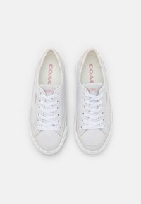 Paire de baskets basses blanches avec lacets, marquage "Coach" rose clair à l'intérieur et sur la languette, présentée sur un fond blanc uni.