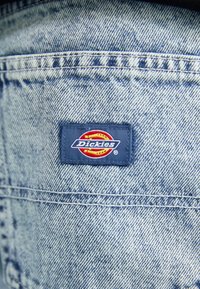 Svetlo modra denim tkanina z vidno tkanino. Značilna je pravokotna mornarsko modra oznaka z rdečim in rumenim krožnim logotipom, ki navaja "Dickies."