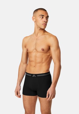 Black boxer briefs with a wide elastic waistband featuring grey stripes, fitted cut, and smooth fabric texture. Model posed sideways.