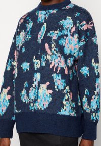 Granatowy sweter z dzianiny z pastelowymi niebieskimi, różowymi i zielonymi wzorami kwiatowymi. Posiada okrągły dekolt oraz ściągacze przy rękawach i u dołu. Miękka struktura.