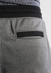 Graue Sportshorts mit einem schwarzen elastischen Bund und einer Gesäßtasche mit schwarzem Akzent. Die Textur ist glatt mit einer melierten Optik.