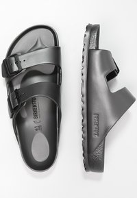 Svarta sandaler med två justerbara spännen, tillverkade av mjukt syntetiskt material, med en formad fotbädd och texturerad sula.