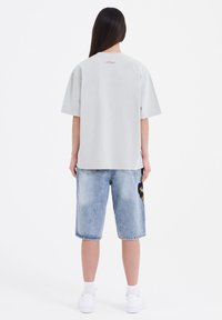 Grå bomulds T-shirt med korte ærmer, sammen med blå denim shorts med et stort sort og guld mærke, båret med hvide sneakers.