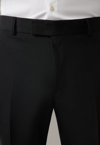 Pantaloni neri in tessuto leggero e liscio, con vita standard, due tasche frontali e design frontale piatto.
