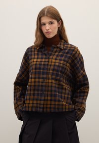 Button-up, checkered flannel shirt in navy and mustard with a collared neckline and relaxed fit. Long sleeves and soft texture.