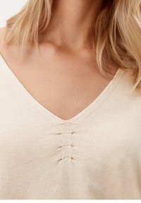 Beige V-Ausschnitt-Oberteil aus weichem Stoff mit dezentem Stichdetail am Ausschnitt. Glatte Textur mit taillierter Silhouette.