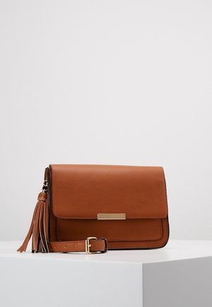 Brązowa skórzana torba na ramię z klapą, złotym prostokątnym zapięciem, regulowanym paskiem i ozdobnym chwostem na białym tle.