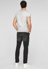 Camiseta gris ajustada combinada con vaqueros de mezclilla negros, con bolsillos traseros y dobladillos enrollados, llevada con zapatillas blancas sobre un fondo claro.