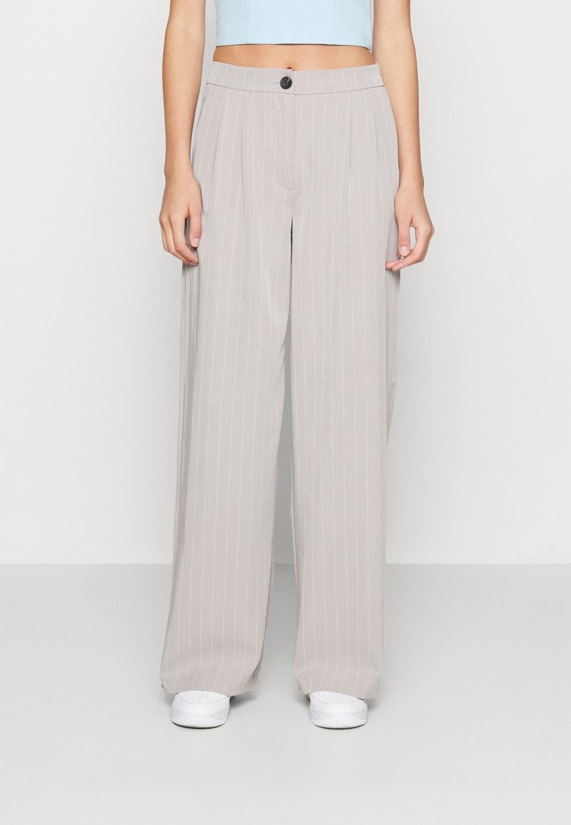 Světle šedé široké kalhoty se svislými pruhy, s jedním tlačítkem na zapínání a hladkým povrchem, nošeny s bílými teniskami.