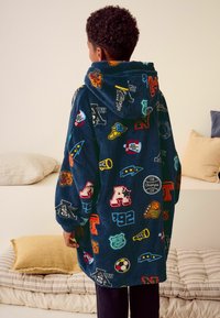 Marineblå fleece-hoodie prydet med farverige sports- og logo-patches. Har en hætte og løse ærmer. Blød tekstur og rummelig pasform.