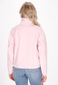 Svetlo roza zip-up jakna z visokim ovratnikom, izdelana iz gladkega, sijočega materiala in raglan rokavi, v kombinaciji z modrimi kavbojkami.