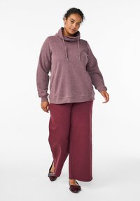 Langärmliger, kapuzenpulli aus weichem, strukturiertem Mauve-Stoff, kombiniert mit weiten burgunderfarbenen Hosen und verzierten Schuhen.
