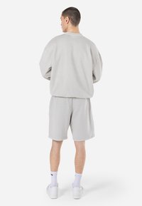 Sudadera de algodón gris claro y pantalones cortos a juego, con un corte relajado y puños acanalados, llevados con zapatillas blancas y calcetines de longitud corta.