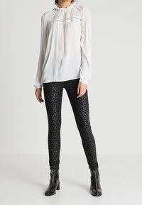 Hvid langærmet bluse med rynket halsudskæring over sorte leggings med en subtil leopardprint, parret med sorte ankelstøvler.