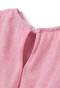 Bluse in zartem Rosa mit Paisleymuster, mit Knopfverschluss am Hals und gewellten Details entlang der Stoffkante.