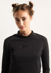 Black long-sleeve top made from soft material, featuring a high collar and subtle embroidered logo on the chest. Smooth texture.