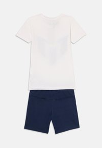 T-shirt blanc à manches courtes avec un motif discret au dos, associé à un short bleu marine présentant une texture lisse et une taille élastique.