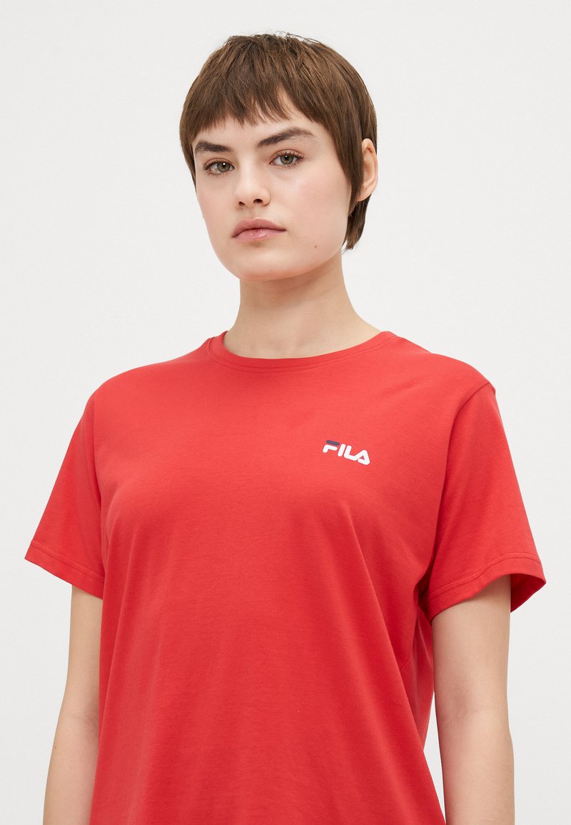 Czerwona koszulka z krótkim rękawem z bawełnianego materiału z białym logo FILA na lewej piersi. Gładka tekstura i klasyczny okrągły dekolt.