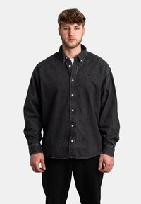 Sort denimskjorte med knaplukning foran, krave og lange ærmer; har et diskret logo, afslappet pasform og tekstureret stof.