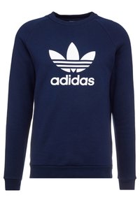 Námořnická modrá mikina vyrobená z bavlněné směsi; na přední straně se nachází velké bílé logo Adidas a design se třemi pruhy. Hladké manžety a lem.