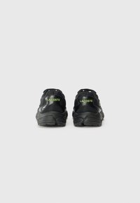 Black sneakers featuring a textured design, prominent heel cushioning, and green Lacoste logo accents on the back. Smooth material finish.