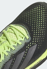 Černá a fluorescentně zelená atletická bota s síťovaným svrškem, unikátním perforovaným designem a texturovanými detaily. Na podrážce je vytištěno "DREAMSTRIKE".