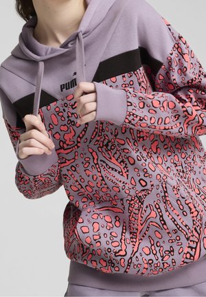 Personne portant un hoodie Puma violet avec des accents noirs et un imprimé animal abstrait rose corail, tenant les cordons du hoodie avec les deux mains.