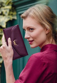 Dark burgundy wallet made of textured leather, featuring a sleek flap, gold-tone hardware detail, and a curved design.