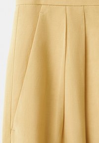 Section de jupe beige avec des plis verticaux et une surface de tissu lisse et texturée.