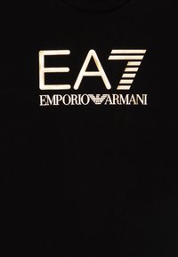 Melns T-krekls ar izteiktu baltu tekstu: "EA7" un "EMPORIO ARMANI" ar stilizētu ērgļa īstumu. Mīksta kokvilnas auduma, ar apaļu kaklu.