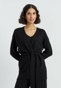 Zwarte lange mouwen cardigan met een V-hals en striksluiting. Gemaakt van zachte stof, met een geribbelde zoom en lange, ontspannen mouwen.