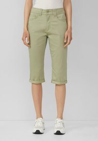 Jasnozielone spodnie typu cropped wykonane z miękkiego materiału o prostym kroju, z podwiniętymi mankietami i kieszeniami z przodu, połączone z białymi trampkami.
