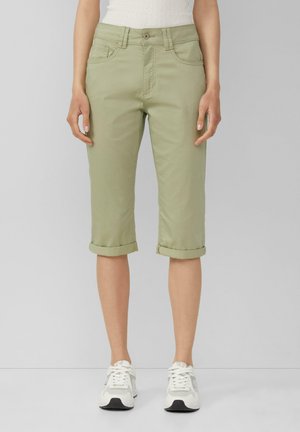 Pantalons court verts clairs en tissu doux avec une coupe droite, présentant des revers et des poches avant, associés à des baskets blanches.