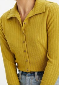 Senapsgul skjorta med krage, texturerade ränder och fem knappar. Matchad med ljusblå högmidjade jeans.