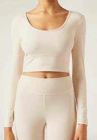 Helles beige Langarm-Crop-Top mit rundem Ausschnitt und nahtlosem Design, kombiniert mit hochtaillierten passenden Leggings. Glatte Textur.