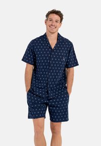 Ensemble de pyjama à manches courtes bleu marine avec un motif léger répétitif, comprenant un col et une poche ouverte sur la chemise.