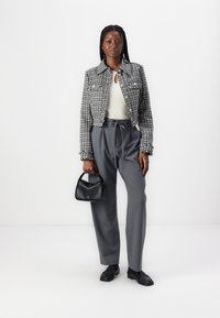 Harmaa tweed-vuorattu lyhyt takki, jossa on hopeanvärisiä nappeja, off-white yläosa, harmaat muotisaumat, ja pieni musta laukku. Mustat kengät viimeistelevät ilmeen.