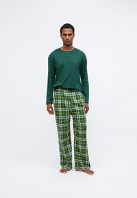 Πράσινο μακρυμάνικο πουκάμισο συνδυασμένο με καρό πιτζάμες σε πράσινο, λευκό και κίτρινο. Οι παντελόνες έχουν ελεύθερη γραμμή και ελαστική μέση.