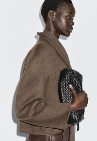 Brown wool-blend oversized cardigan with wide sleeves, paired with a black woven clutch. Smooth texture against a plain white background.