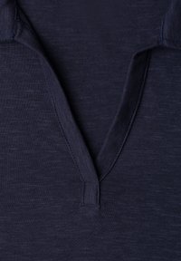 Gros plan d'un tissu bleu marine foncé avec un col en V et des détails de couture visibles.