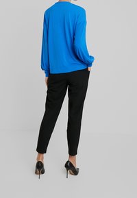 Långärmad ljusblå topp i kombination med svarta avsmalnande byxor och svarta stiletto-klackar, som visar en avslappnad passform och en mjuk tygtextur.