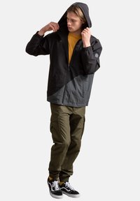 Zwart en grijs zip-up jack met capuchon, gecombineerd met olijfgroene cargo pants en zwarte sneakers. Kenmerken zijn elastische manchetten en een relaxte pasvorm.
